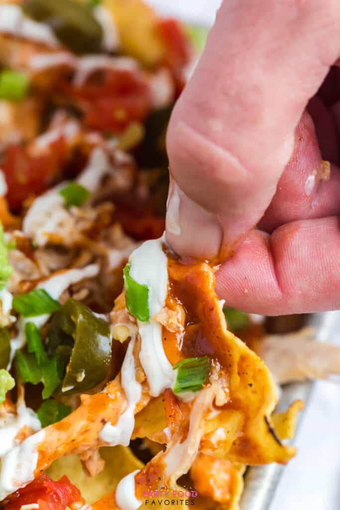 lifting a nacho covered with sour cream and beer cheese