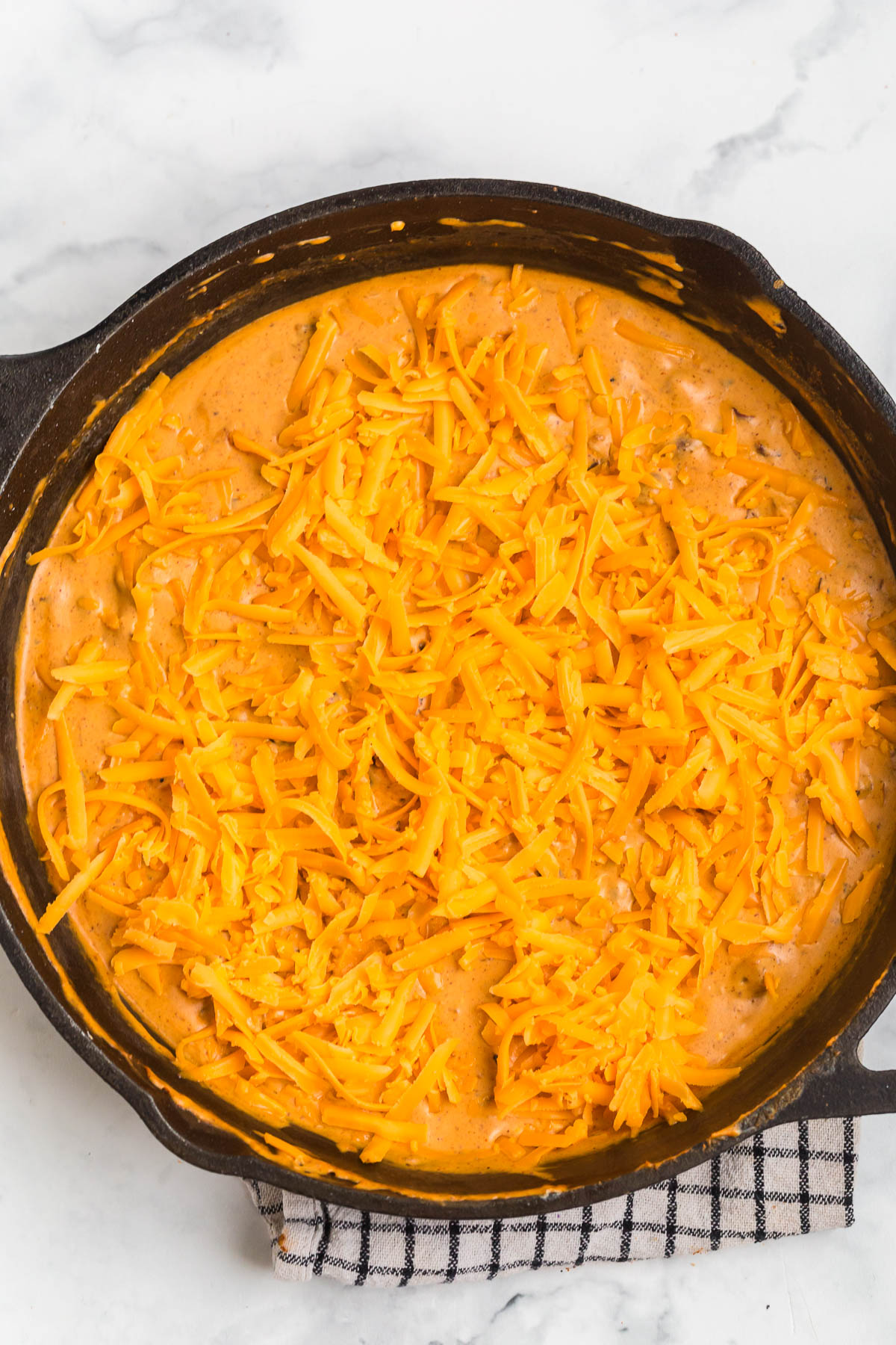shredded cheddar cheese in a cast iron pan about to go in the oven