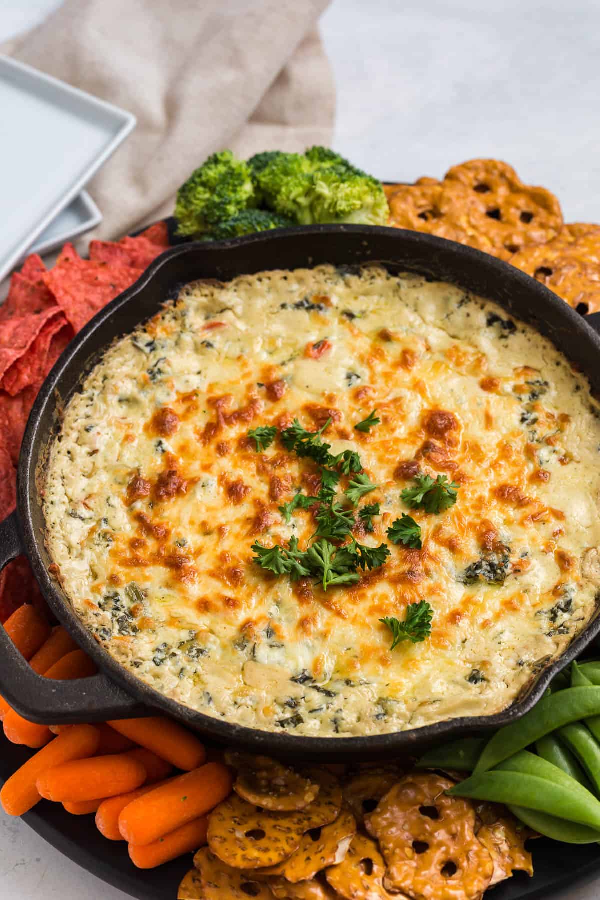 cheesy baked spinach dip with colored tortilla chips, vegetables, and pretzel chips