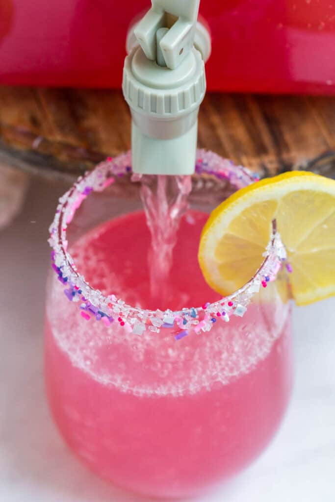 a rimmed glass with sprinkles and pouring party punch