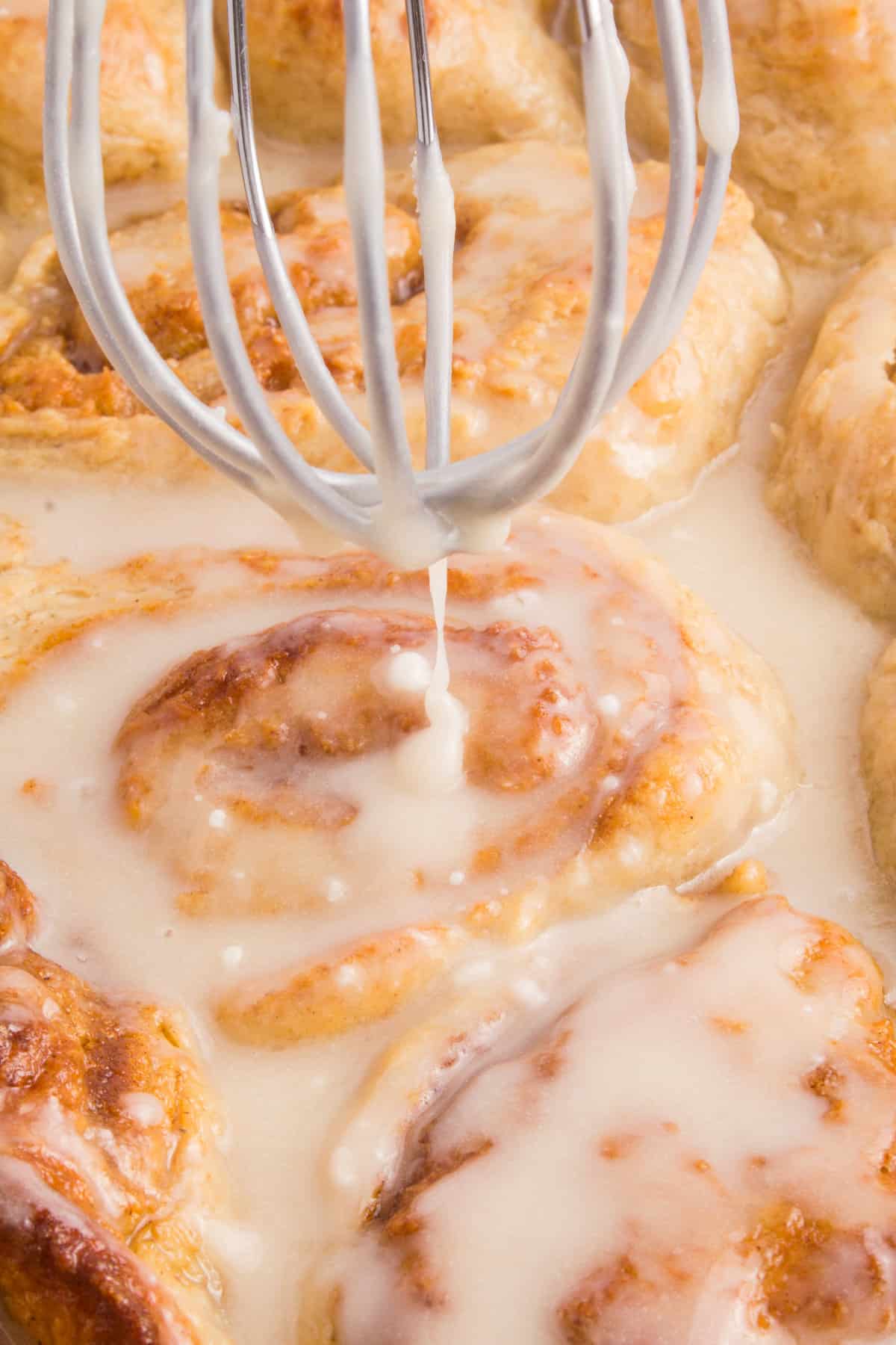 drizzling cream cheese icing over cinnamon rolls